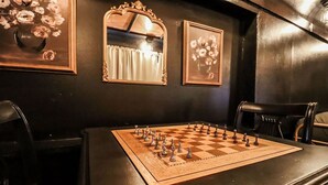 Ein Schachbrett auf einem Tisch, mit einem Spiegel und einem gerahmten Blumenbild an der Wand.