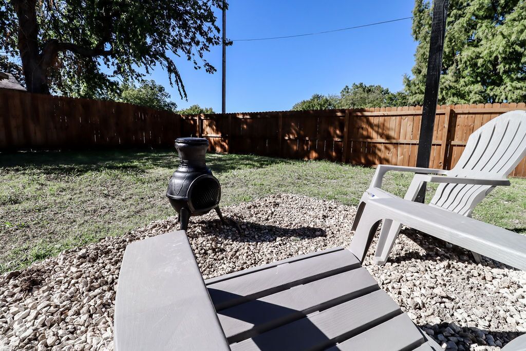 Eine Terrasse mit Grill, Adirondack-Stuhl und einem Holzzaun im Hintergrund.