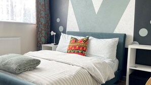 A modern bedroom with a bed, a nightstand, a dresser, and a large window with curtains. - 
Penn Gardens - Two Bedroom Apartment (Romford, Greater London, United Kingdom)