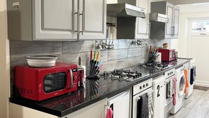 A modern kitchen with grey cabinets, a red microwave, a gas stove, and a built-in washing machine. - 
Penn Gardens - Two Bedroom Apartment (Romford, Greater London, United Kingdom)