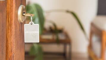 Una puerta con un ojo de cerradura y una llave insertada, un letrero con la inscripción “LOS GUINDOS APART” visible, y un fondo desenfocado con una planta.