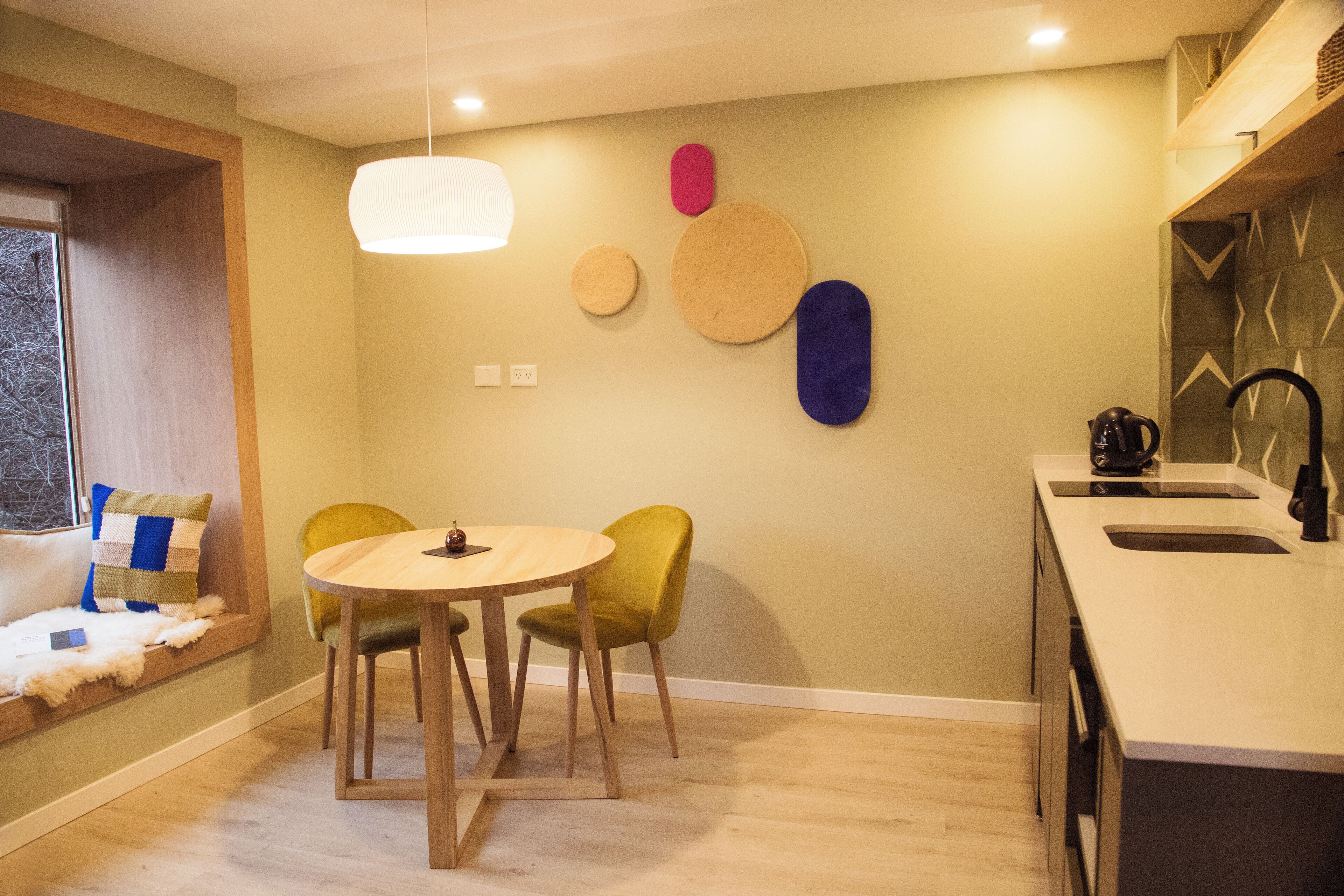 Una cocina moderna con una mesa redonda de madera y dos sillas, un lavamanos empotrado y un ventanal con vistas.