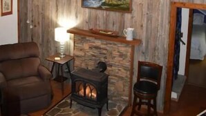 A cozy room with a wooden wall, a fireplace, a comfortable chair, and a table with a lamp.