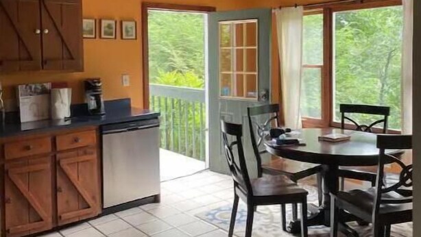 A kitchen with wooden cabinets, a dining table with chairs, and a view of the outdoors through large windows.