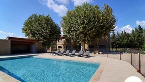 A swimming pool with lounge chairs, a covered area, and a building with a tiled roof in the background. - Gîte Spacieux, Rénové, Climatisé Avec Grande Piscine Sécurisée, Jardin Clos (Châteaurenard)