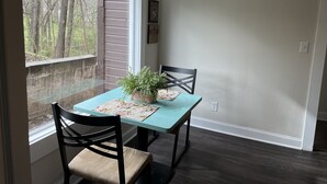 A dining area with a table and chairs, a window with a view of trees, and a wall with a picture. - Garden House, Unit B (Hot Springs)
