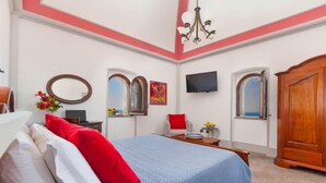 A bedroom with a bed, a wooden wardrobe, a TV, and a desk with a chair.