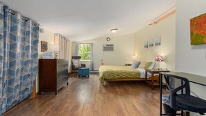 A bedroom with a bed, a desk, a chair, a dresser, and a window with curtains.