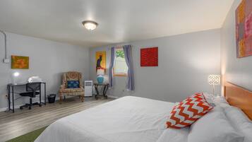 A hotel room with a bed, a desk, a chair, a window, and a ceiling light.