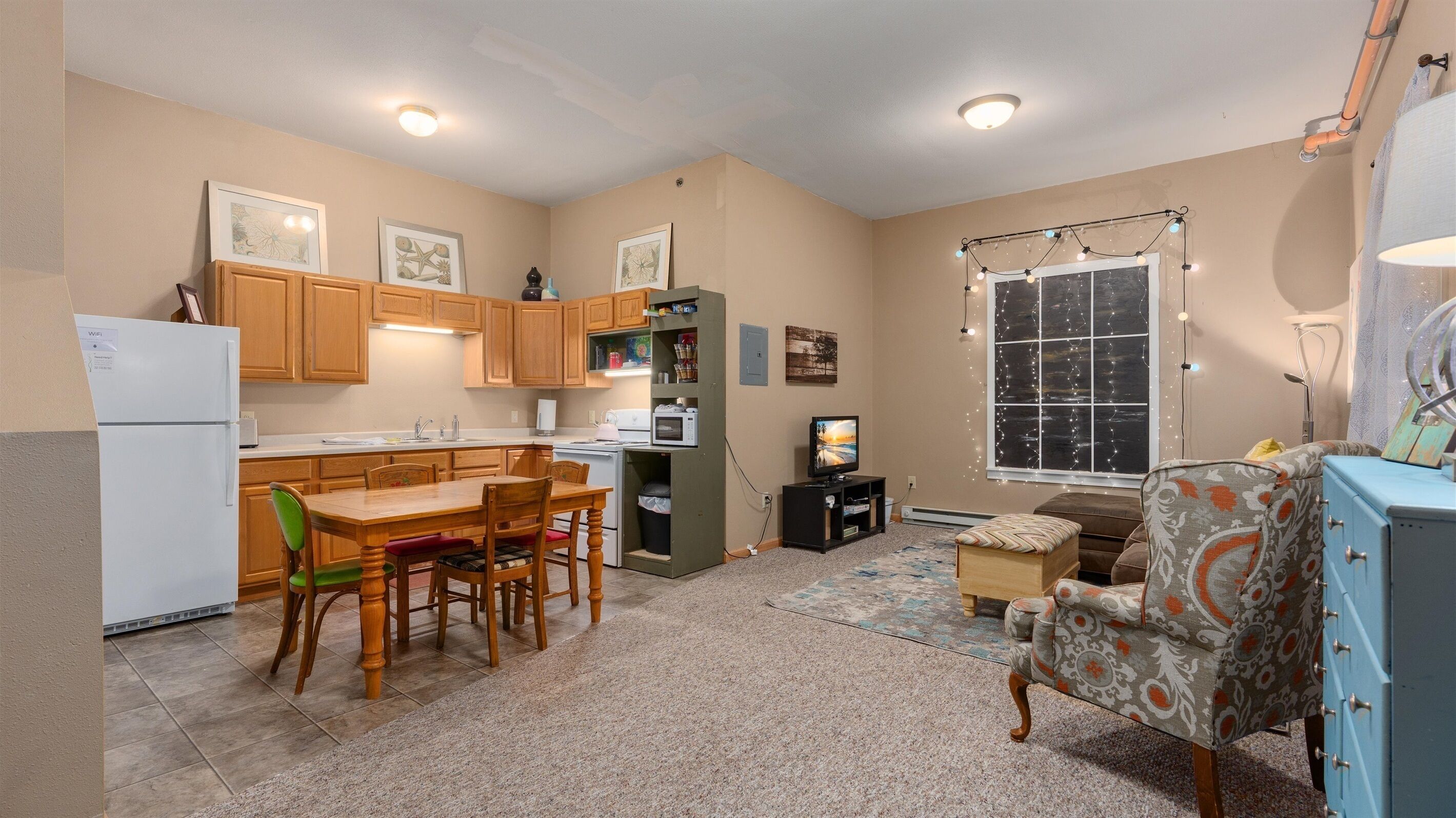 A compact kitchen with wooden cabinets, a dining table with chairs, a refrigerator, a microwave, and a television.