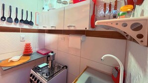 Een compacte keuken met een gasfornuis, een spoelbak en diverse keukengerei dat erboven hangt.