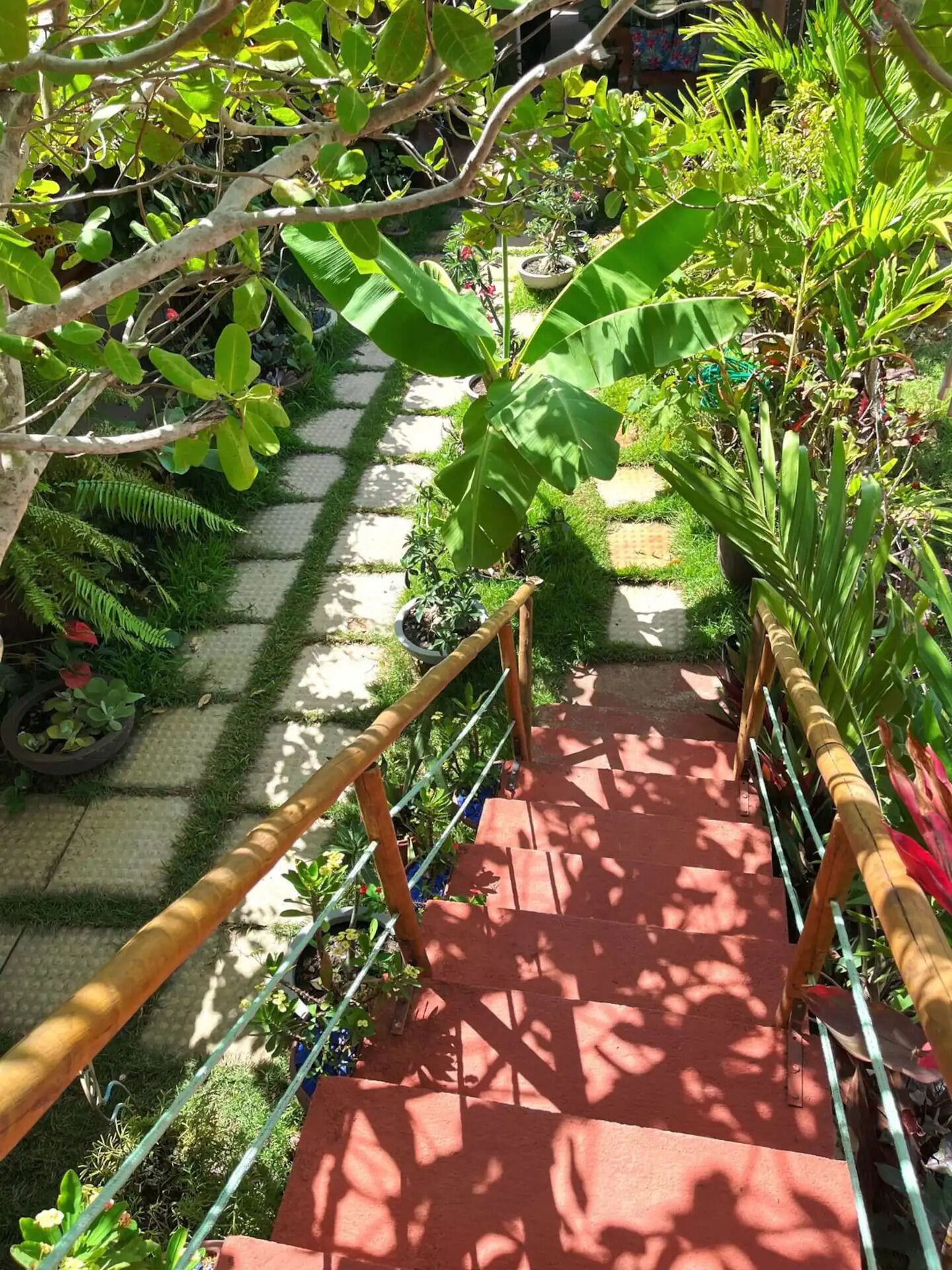 A wooden staircase with a metal railing leading to a garden area with various plants and a paved path.