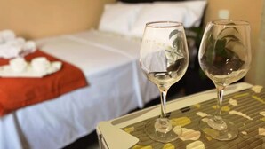 Een hotelkamer met een net opgemaakt bed, een tafel met twee wijnglazen en een plantje op de achtergrond.