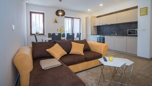 A modern living room with a brown sofa, a small white table, and a kitchen in the background. - Two bedroom apartment Milohanic III (Porec)