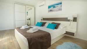 A modern hotel room with a large bed, a headboard with a built-in TV, a painting of a beach scene, and a fluffy blue rug. - Two bedroom apartment Milohanic III (Porec)