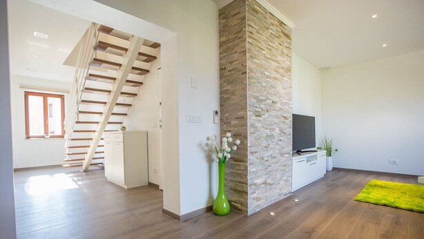 Ein geräumiger Wohnbereich mit einer Holztreppe, einer Wand aus Naturstein, einem Flachbildfernseher und einem leuchtend grünen Teppich.