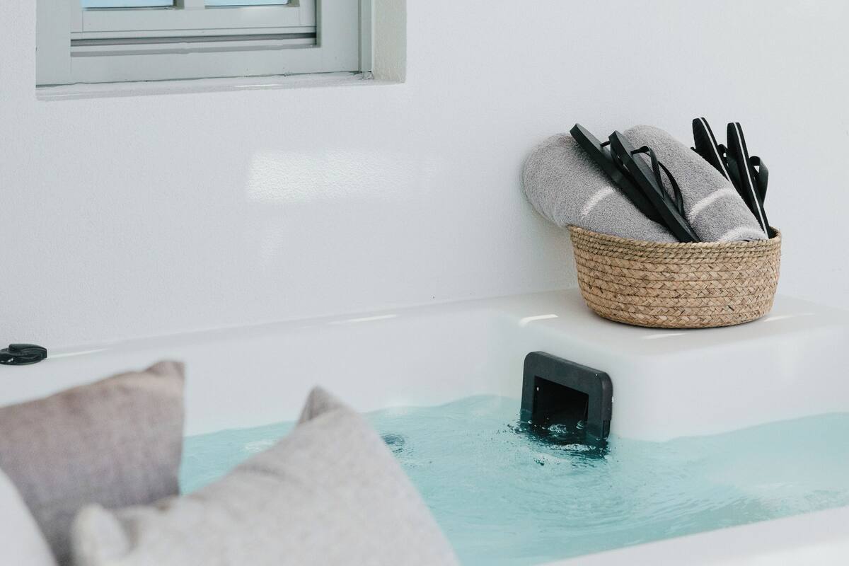 A modern bathroom with a bathtub, a window, and a basket of toiletries.