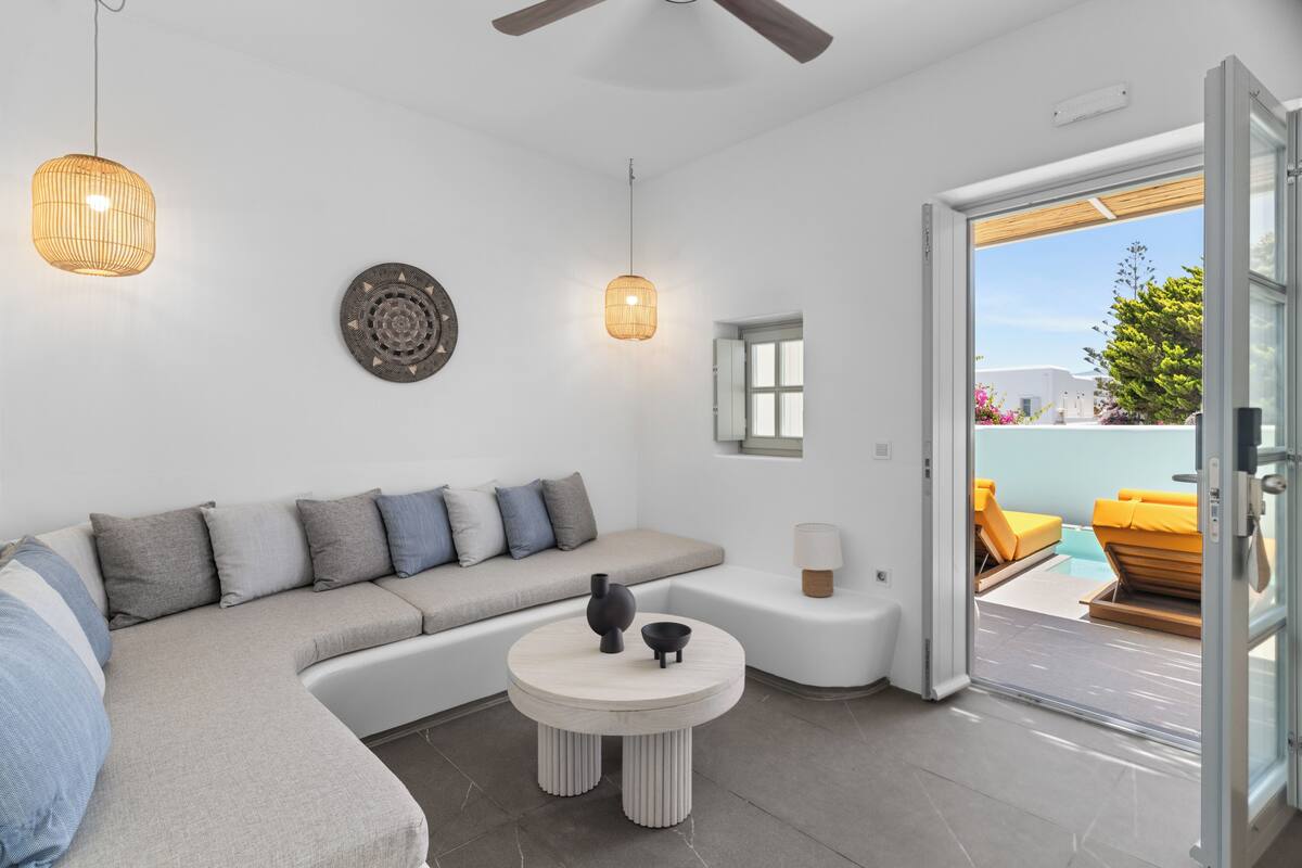 A modern, well-lit room with a sofa, a round table, and a view of an outdoor seating area.