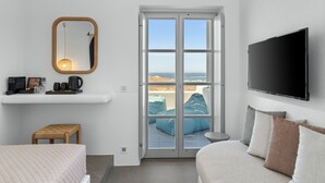 A modern hotel room with a bed, a seating area with cushions, a television, a mirror, and a balcony with a view. -  Mr and Mrs White Paros Suites and more (Paros)