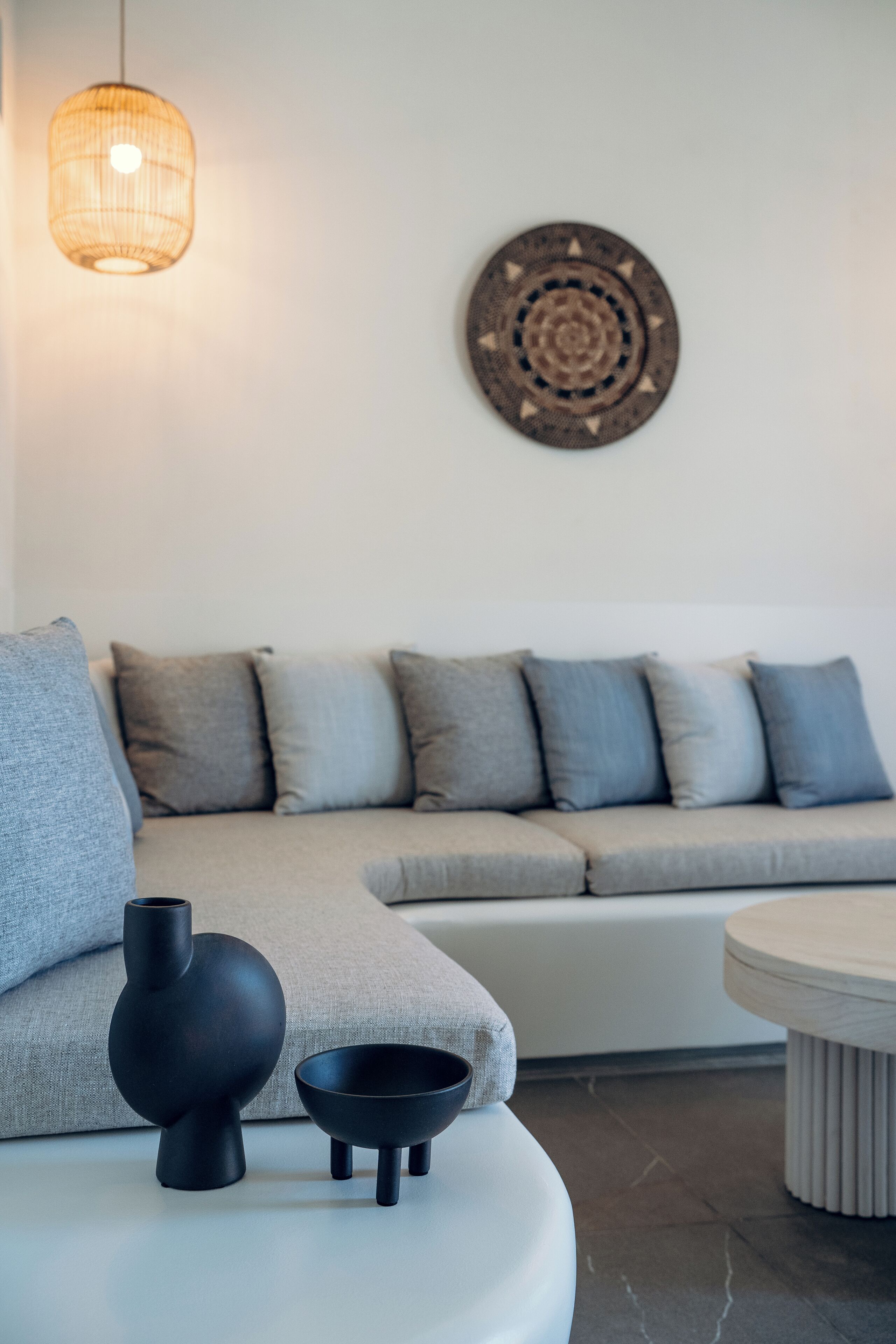 Un salon moderne avec un canapé d’angle gris, un vase noir et un bol posé sur un pouf blanc.