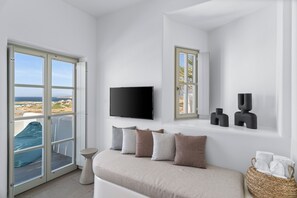 A modern bedroom with a large window, a flat-screen TV, and a sofa with multiple cushions. -  Mr and Mrs White Paros Suites and more (Paros)