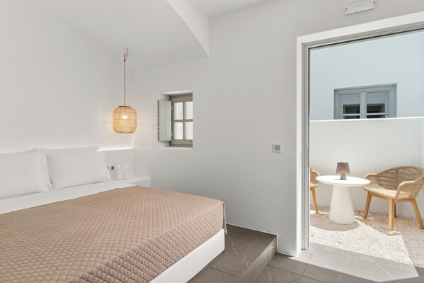 A modern bedroom with a large bed, a hanging light fixture, a small window, and a balcony with wicker furniture. -  Mr and Mrs White Paros Suites and more (Paros)