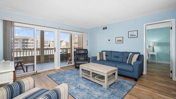 Un salon avec un canapé bleu, un divan à rayures, une table basse et une vue sur l’extérieur grâce à de grandes portes-fenêtres coulissantes.