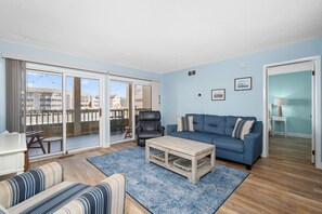 A living room with a blue sofa, a striped couch, a coffee table, and a view of the outside through large sliding glass doors.