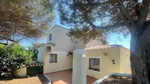 Un bâtiment à deux étages, dot é d’un toit en tuiles, d’un petit jardin et d’un arbre au premier plan.