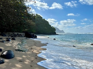Uma praia com costa rochosa, céu azul límpido e montanhas ao longe.