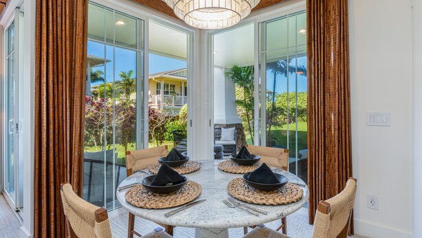 A dining area with a round table, four chairs, and a view of a tropical landscape through large glass doors.