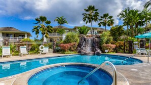 A swimming pool with a waterfall feature, surrounded by palm trees and lounge chairs.