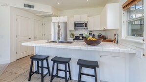 A modern kitchen with white cabinetry, a stainless steel refrigerator, a microwave, and a large island with stools.