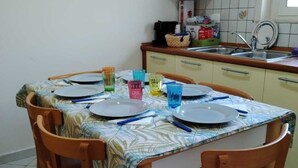 A dining table set with plates, glasses, and cutlery in a kitchen with wooden cabinets and a tiled backsplash.