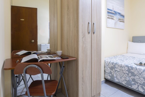 A bedroom with a bed, a desk with a chair, a wardrobe, and a painting on the wall.