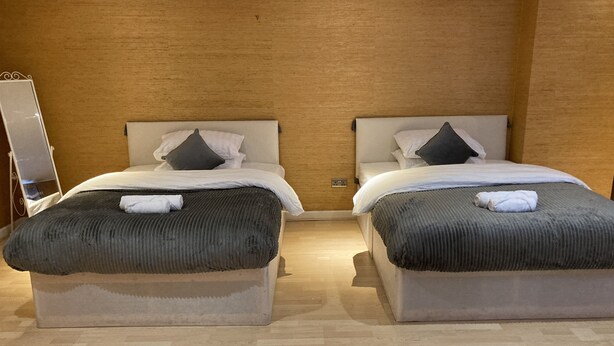 Een hotelkamer met twee bedden, elk met hoofdbord, een spiegel en een houten vloer.