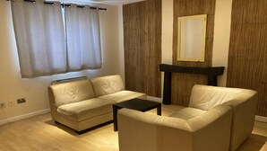 Een woonkamer met een beige bank, een zwarte salontafel en een houten accentmuur.