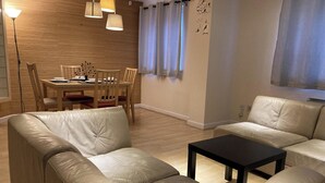 Een woonkamer met een bank, een salontafel, een eettafel met stoelen, hanglampen en een raam met gordijnen.