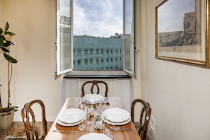 A dining area with a table set for four, a window with a view of buildings, and a framed picture on the wall.