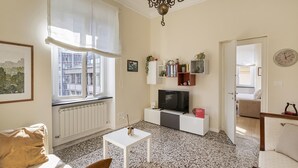 Uma sala de estar com um sofá branco, uma mesa de centro, uma televisão e uma estante de livros.