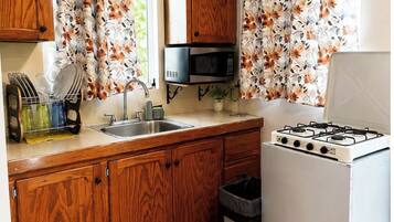 A compact kitchen with wooden cabinets, a microwave, a sink, and a gas stove.