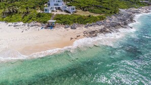 Een pand aan het strand met een groot huis, een zandstrand en helder turquoise water.