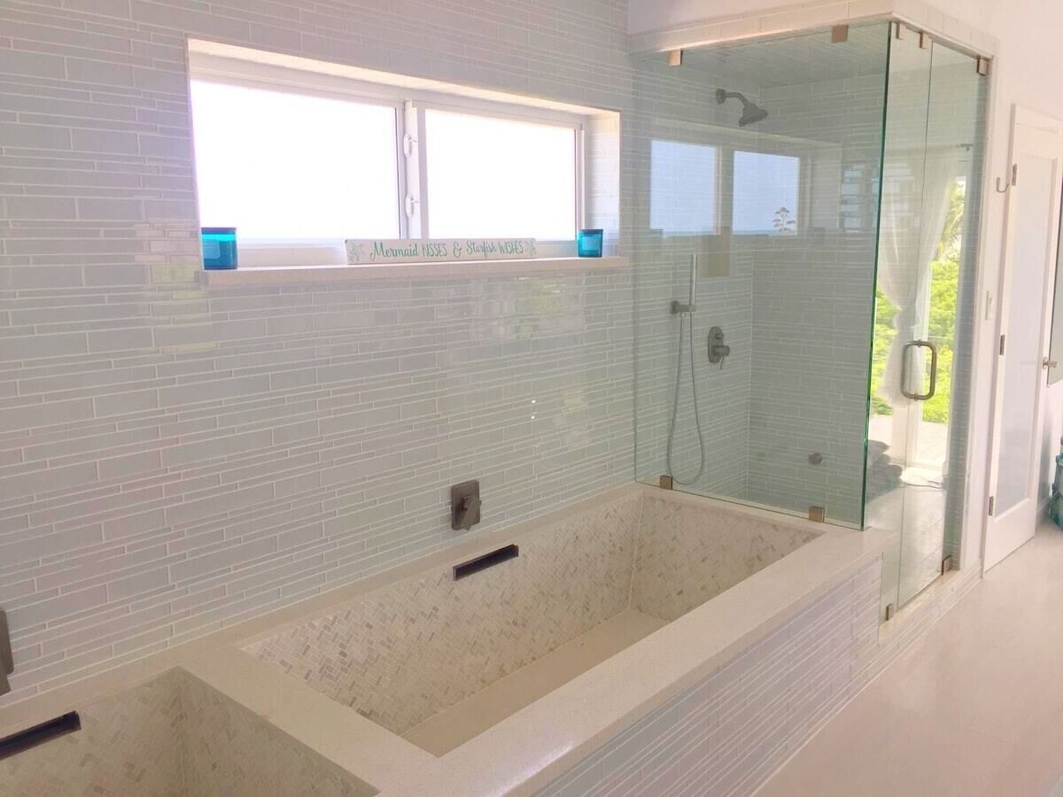 A modern bathroom with a large bathtub, a glass-enclosed shower, and a window with a sign above it.