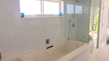 A modern bathroom with a large bathtub, a glass-enclosed shower, and a window with a sign above it.
