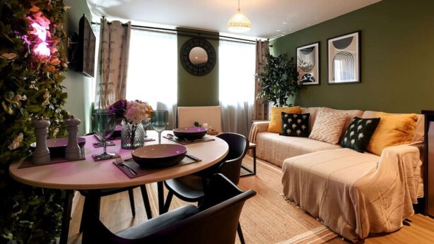 Ein gemütliches Wohnzimmer mit einer Couch, einem Esstisch mit Stühlen, einer Topfpflanze und einem Wandspiegel.