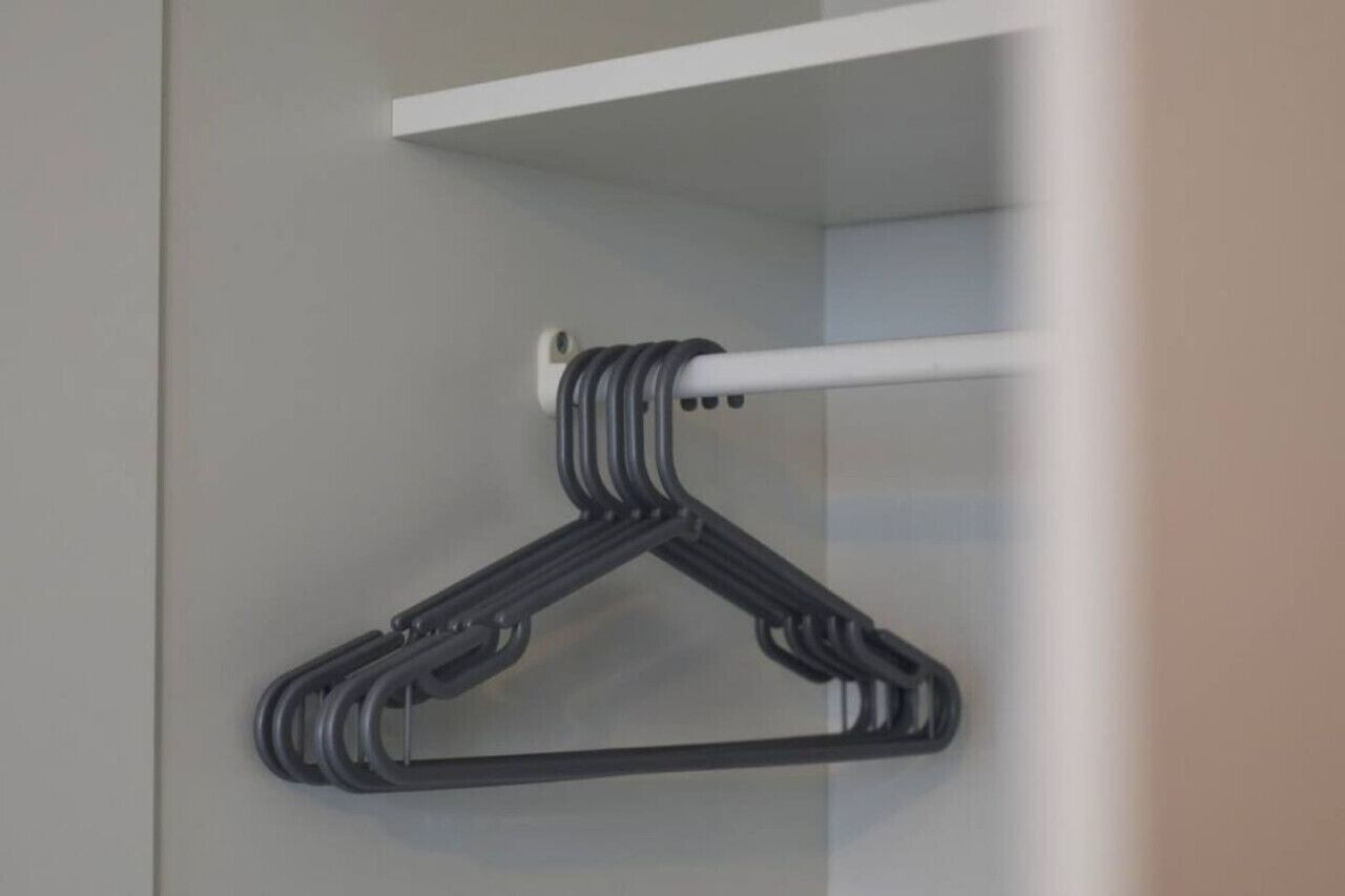 A black hanger on a white wall-mounted rod in a room with a grey wall and a white shelf above.