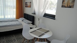 Een hotelkamer met een bed, een kleine tafel met stoelen, een raam met gordijnen, en twee aan de muur hangende schilderijen.