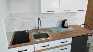 Een moderne keuken met witte kasten, een roestvrijstalen spoelbak, een waterkoker en een zwart inductiefornuis.