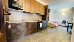 A modern kitchen with wooden cabinets, a built-in oven, and a microwave. There is a dining area with a table and chairs. - Residence VILLA LINDA (Bardonecchia)