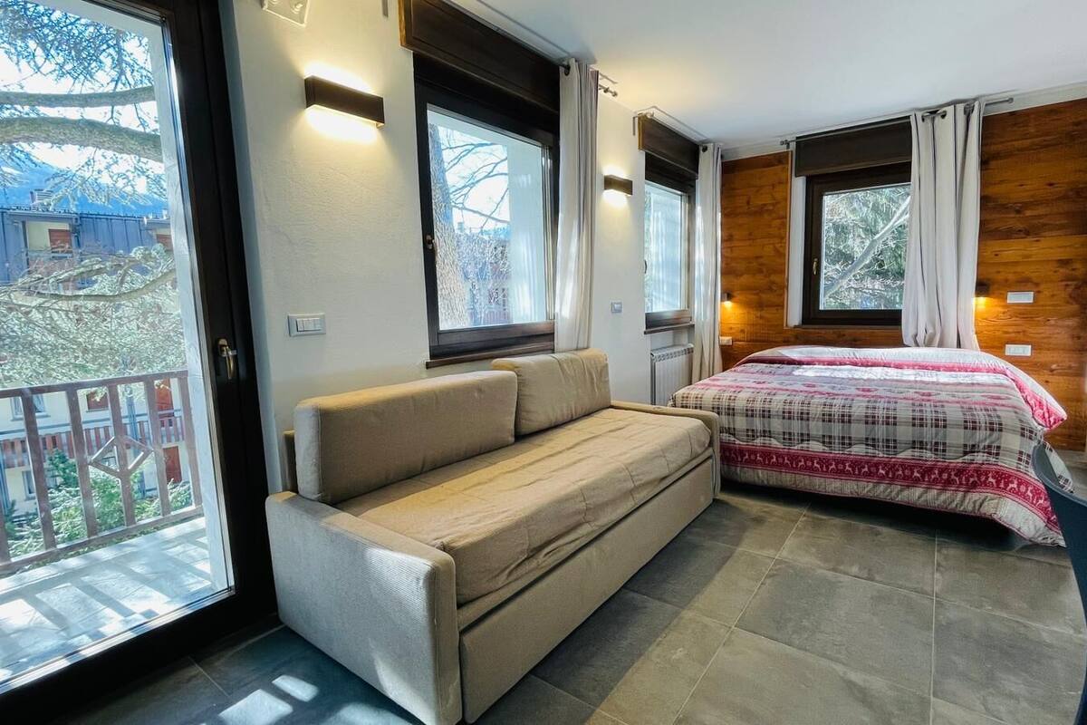 A cozy room with a sofa and a bed, large windows, and a view of the outside.
